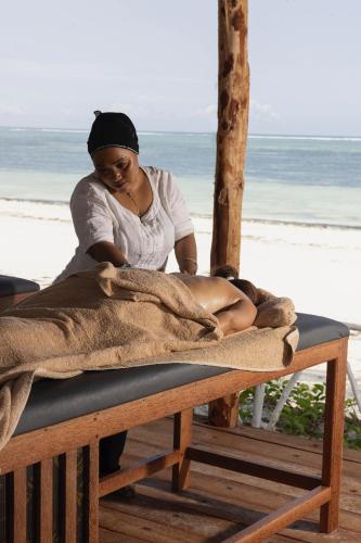 a woman sitting on a bed on the beach at ZAN Orient Beach Hotel in Bwejuu