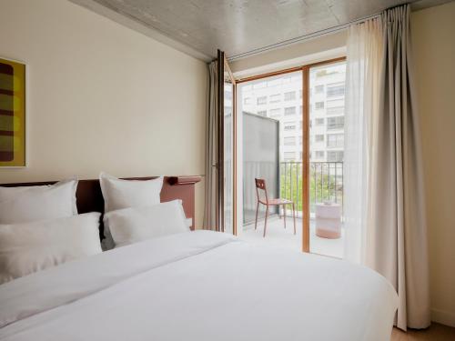 a bedroom with a large white bed and a balcony at Edgar Suites - Église in Paris