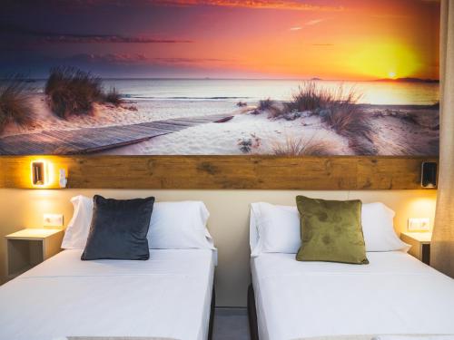 two beds in a room with a picture of the beach at Huelin Edificio Apartamentos in Málaga
