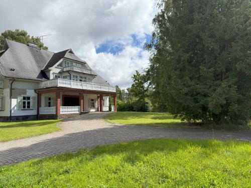 a large white house with a tree and a driveway at Atpūtas komplekss "Ratnieki" in Ratnieki