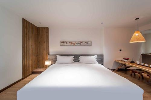 a bedroom with a large white bed and a desk at Dujiangyan Irrigation Project Puruna Hot Spring Hotel Panda Valley Store in Dujiangyan