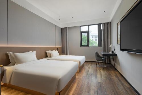 two beds in a hotel room with a flat screen tv at Urbain S Hotel, Xiamen Railway Station Mingfa Commercial Plaza in Xiamen
