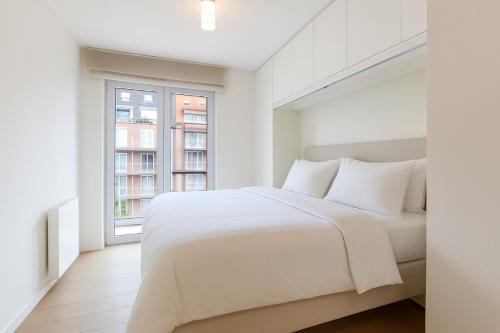 ein weißes Schlafzimmer mit einem großen Bett und einem Fenster in der Unterkunft Koningslaan Zegemeer Knokke in Knokke-Heist
