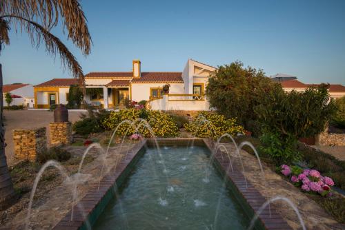 a swimming pool with a fountain in front of a house at Herdade do Amarelo Nature & Spa in Vila Nova de Milfontes