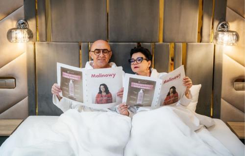 two people sitting in a bed reading newspapers at Malinowy Dwór Hotel Medical SPA in Świeradów-Zdrój