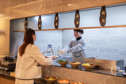 Atour Hotel Xuzhou Chuangtuo Aofan Mining University في سوزهو: امرأة تقف في مطبخ تقوم باعداد الطعام