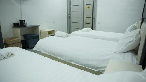 two beds in a room with white sheets at Lotus Hotel in Yakkasaray