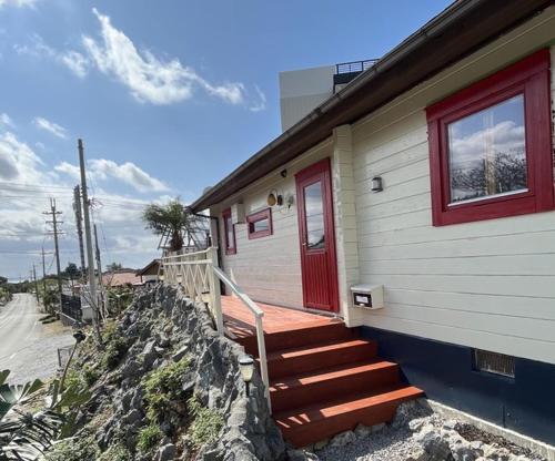 a house with a red door and stairs on it at Sesoko Log Cabin [Chimu lani] - Vacation STAY 26745v in Sesoko