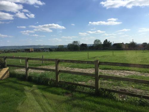 a wooden fence in a field with a green pasture at Rew Farm Country & Equestrian Accommodation - Sunrise Lodge in Melksham