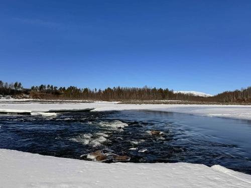 a river with snow and trees in the background at Målselvfossen Feriesenter in Bardufoss