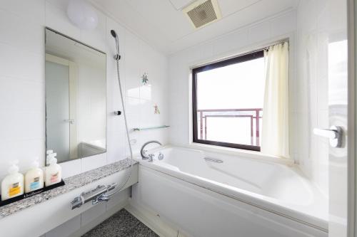 a white bathroom with a tub and a window at Hotel BELLMARE ホテルベルマーレ in Maizuru