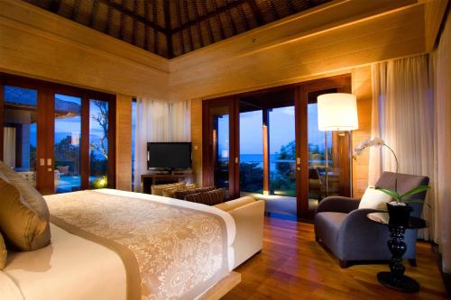 a bedroom with a bed and a chair and windows at Conrad Bali in Nusa Dua