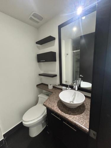 Un baño con inodoro, lavabo y espejo. en Loft la Carolina, en Quito