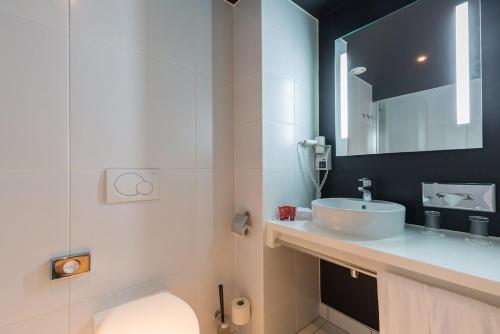 a bathroom with a sink and a toilet and a mirror at Leonardo Hotel Almere City Center in Almere
