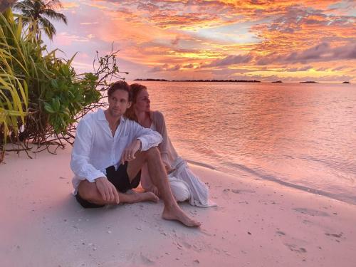 a man and woman sitting on the beach at sunset at Oceanic Inn in Kolamaafushi