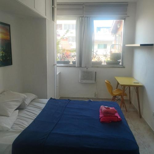 a bedroom with a blue bed with a table and a window at Cobertura posto 5 in Rio de Janeiro