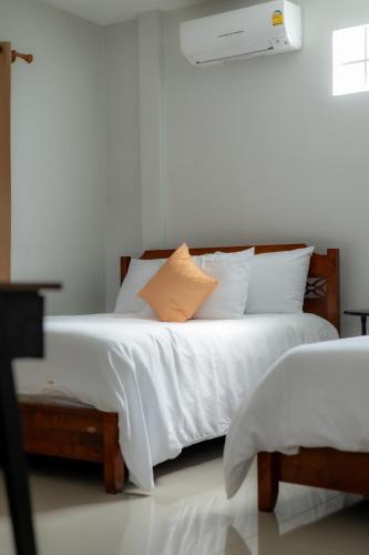 a bed with white sheets and an orange pillow on it at Gita's House in Chiang Rai