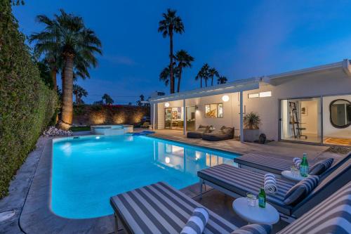 a swimming pool with two benches and a house at Mid Century Mood House by ACME House Company in Palm Springs