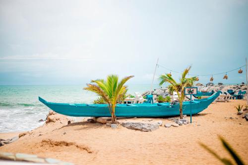 a blue boat on a beach with palm trees at Oasis beach resort in Cape Coast