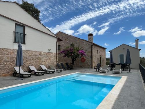 a swimming pool with chairs and umbrellas next to a building at Quinta do Carvalho Cerquinho in Louriceiras de Baixo