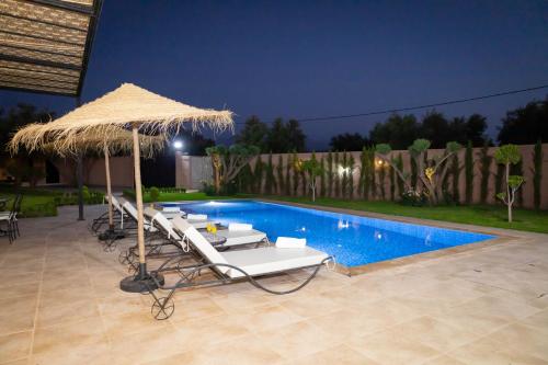 a pool with lounge chairs and a straw umbrella at Villa Privée de Luxe avec Piscine et Vue sur l Atlas Marrakech in Aghmat