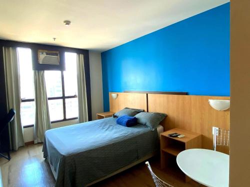 a bedroom with a blue wall with a bed and a table at Flat Particular Hotel Confort Taguatinga in Taguatinga