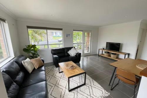 a living room with a black leather couch and a table at Sea Salt One Burgess Beach in Forster