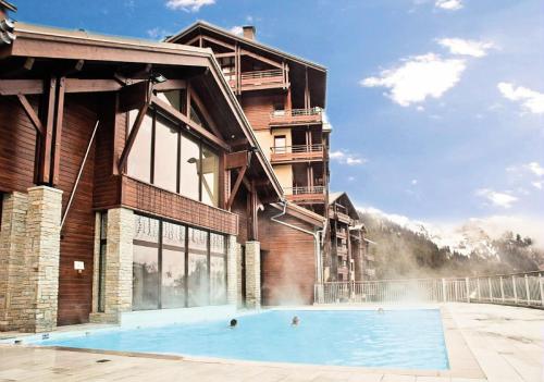 a hotel with a swimming pool in front of a building at Résidence Les Terrasses D'eos - Appartement confortable · Accès direct aux pistes · Piscine · Spa · WIFI gratuit et illimité MAE-6164 in Magland