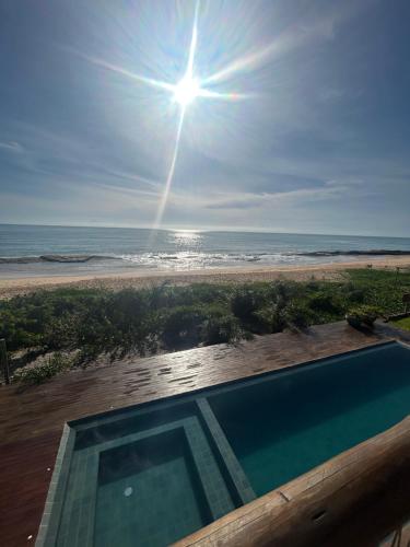 a swimming pool next to a beach with the sun at Kamaiurá Pousada in Caraíva