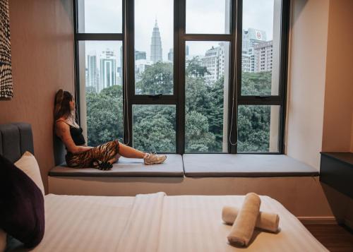 クアラルンプールにあるCeylonz KLCC by Mana-Manaの窓側の座席に座って市街を眺める女性