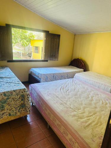 drei Betten in einem Zimmer mit Fenster in der Unterkunft Sítio do Ademir in Jaboticatubas