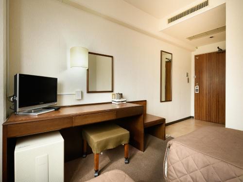 a room with a desk with a television and a bed at ホテル亀山ヒルズ in Kameyama