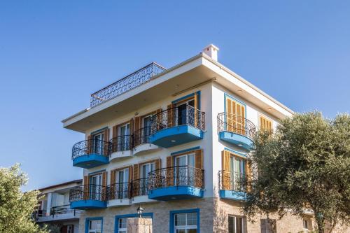 a white building with blue balconies and trees at Clementin Suits Sigacık in Siğacık