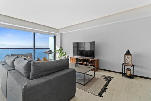 a living room with a gray couch and a large window at Beachfront and modern getaway in Bucerías