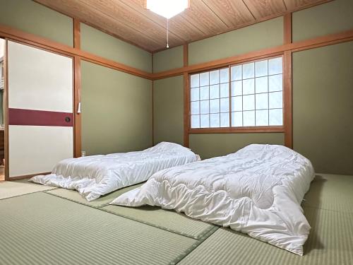 a bed with white sheets in a room with two windows at Summer Cool Forest Cottage-北軽井沢 夏涼の森コテージ- in Tsumagoi