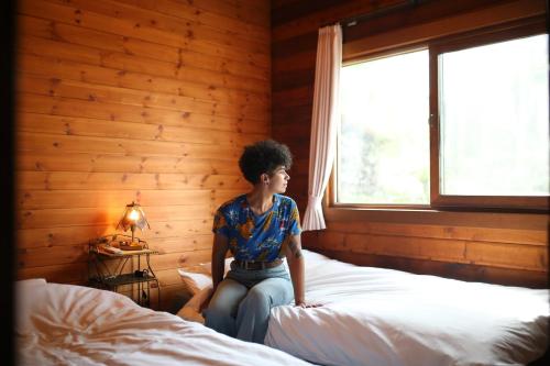 a woman sitting on a bed in a room with a window at Renesto aHOLIDAYHOME - Vacation STAY 27907v in Kobe