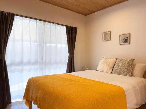 a bedroom with a bed with a yellow blanket and a window at Aizanso - Vacation STAY 22208v in Nakijin