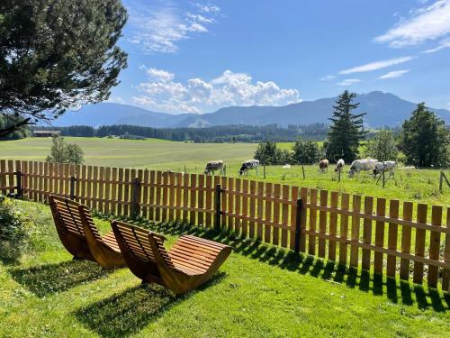 Dos bancos sentados frente a una valla con animales en un campo. en Alpen Panoramahof, en Nesselwang