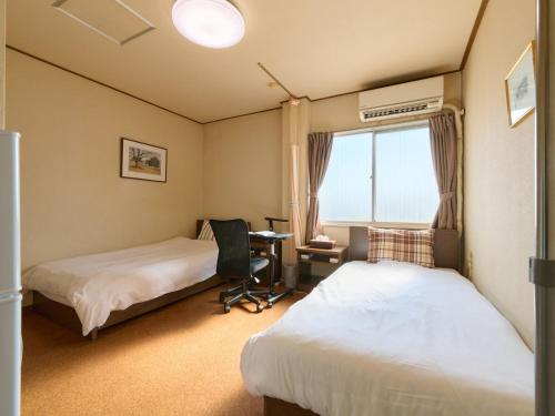a room with two beds and a desk and a window at Tabist Business Hotel Teramoto in Chita
