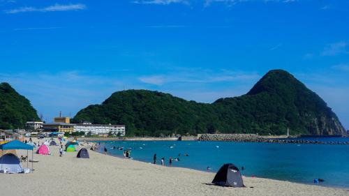 a beach with people in the water and mountains at Base House Kinosaki お子様無料でサウナもアクティビティも楽しめる一棟貸し宿Private Japanese Villa Stay with Free Shuttle, Sauna, Activities & Kids Stay Free in Toyooka