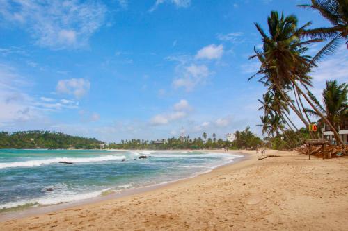 a sandy beach with palm trees and the ocean at Amible Guest Home in Mirissa