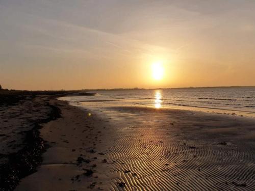 a beach with the sun setting in the ocean at 6 person holiday home in Gørlev in Gørlev