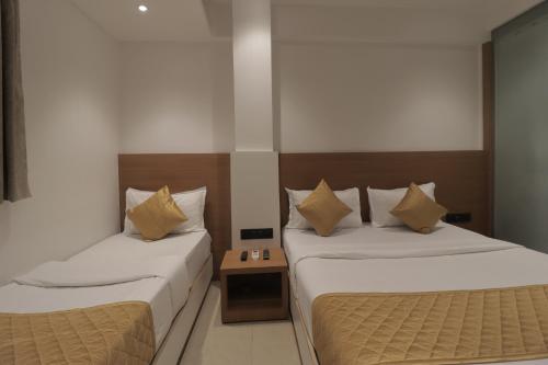 two beds in a hotel room with a table at Hotel Malad Inn opposite Malad Railway Station in Mumbai