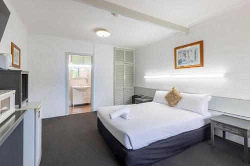 a white bedroom with a bed and a television at The Grampians Motel in Halls Gap
