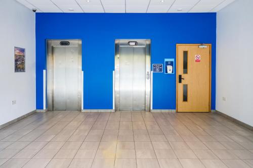 three elevators in a room with a blue wall at GO2 Lancaster Centre Hotel by OYO in Lancaster