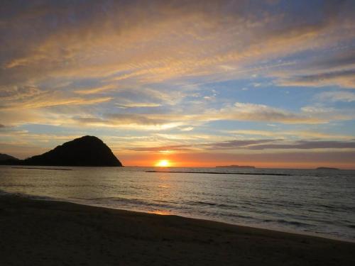 a sunset on the beach with a rock in the water at Hagi no Oyado Hananari no Niwa - Vacation STAY 16121 in Hagi