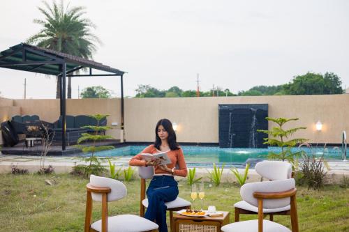 a woman sitting on a chair in front of a pool at The Bliss Nestlewood 2-BHK Villa With Private Pool, Lush Garden & Poolside Gazebo in Udaipur