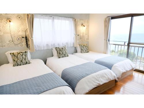 trois lits dans une chambre avec une grande fenêtre dans l'établissement Cottage Umigame no Mieru Yado - Vacation STAY 51905v, à Wadomari