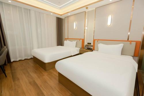 two beds in a hotel room with white sheets at 万信至格酒店乌鲁木齐机场德港万达店 in Ürümqi