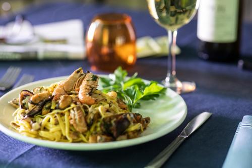 a plate of pasta with chicken and mushrooms and a glass of wine at Amadei Hotel Blumen in Pesaro